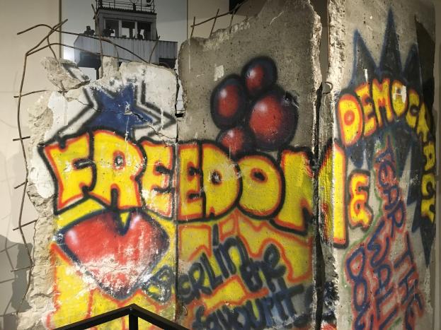 Graffiti auf einer Wand, das in großen schwarzen Buchstaben "Freiheit und Demokratie" liest, mit einem Geländer unten und einem Gebäude mit Fenstern im Hintergrund.