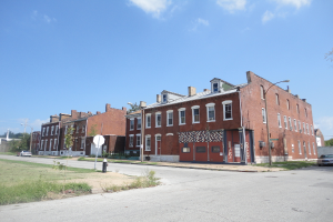 Ein Gebäude mit Masten und Straßenlaternen, umgeben von Bäumen und Fahrzeugen auf beiden Seiten, mit einem Gehweg, Gras und einem Feuerlöscher unten und dem Himmel oben.