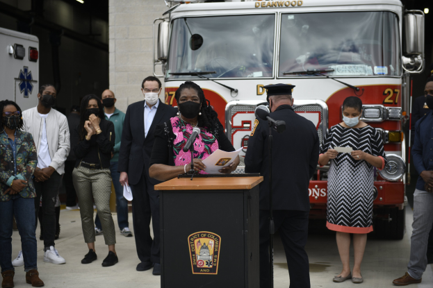 Bürgermeisterin von Chicago Lori Lightfoot spricht bei einer Pressekonferenz vor einem Feuerwehrauto, mit einer maskierten Menge und Podiumsausrüstung im Hintergrund.