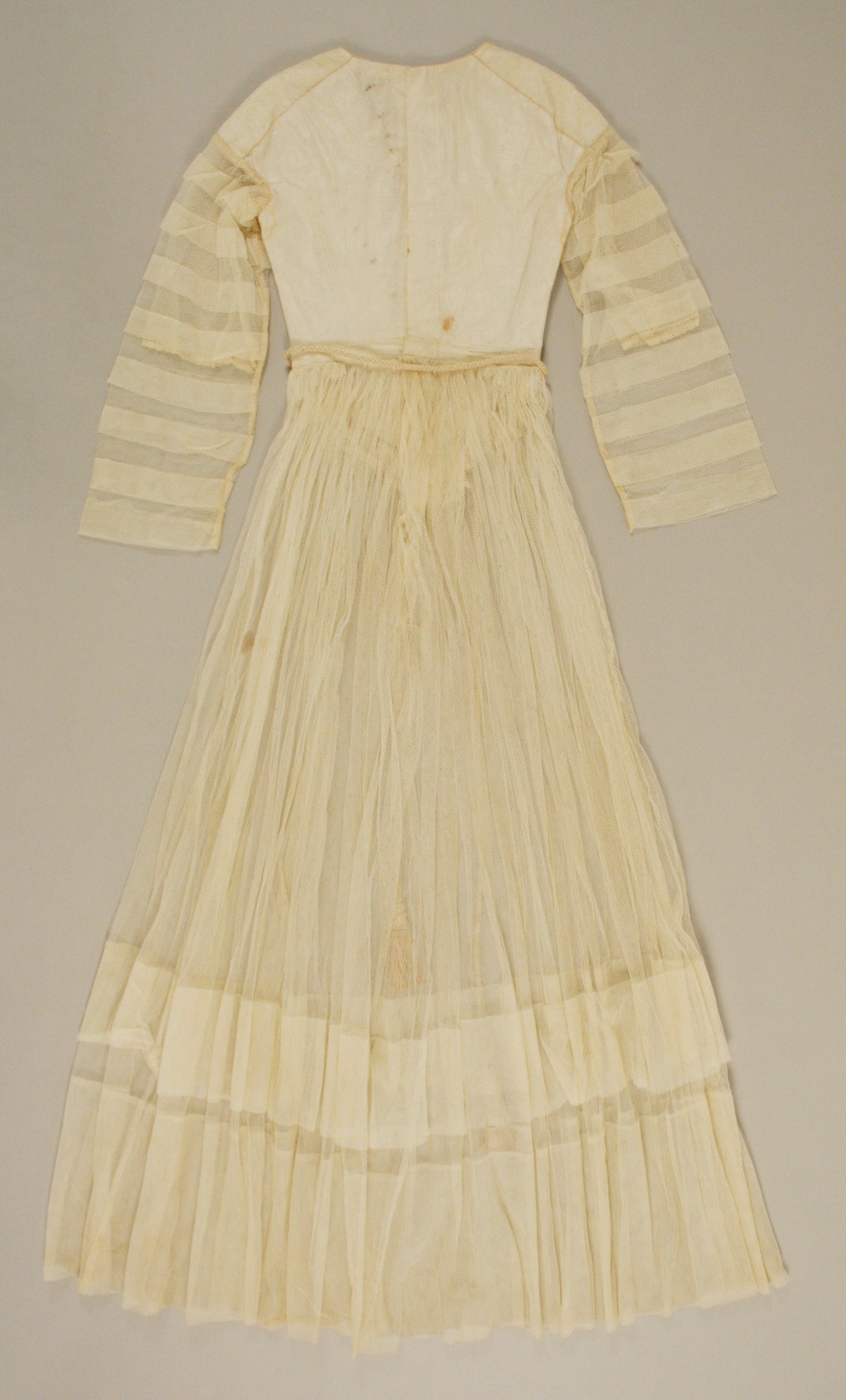 Ein weißes, langärmeliges Kleid mit einer gerüschten, bodenlangen Röcke auf einem weißen Hintergrund, mit hohem Bund und dezentem Schimmer.