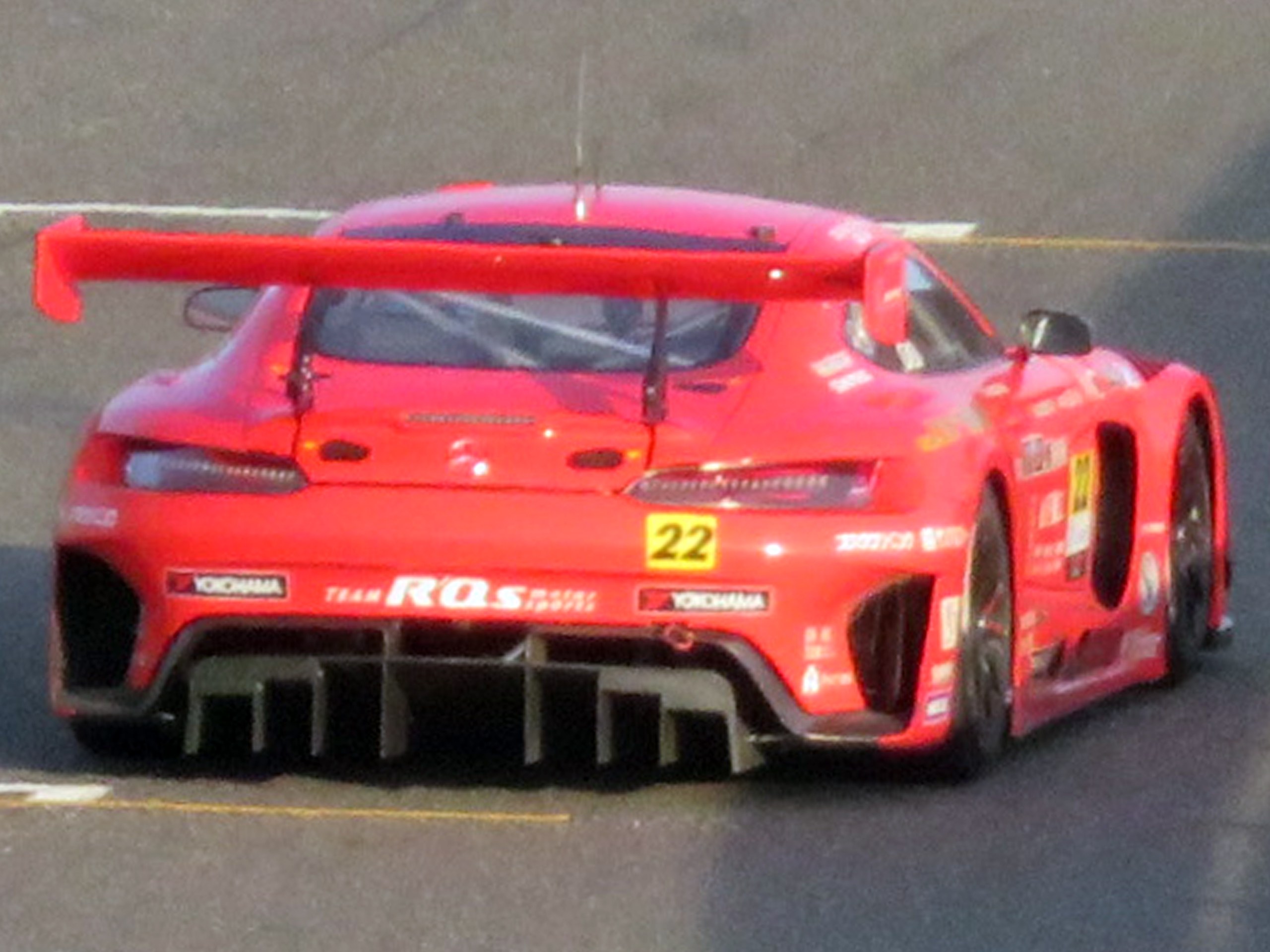 Roter Porsche 911 GTS Rennauto auf einer Rennstrecke mit aerodynamischem Design, großem Heckflügel und schwarzen Rädern.