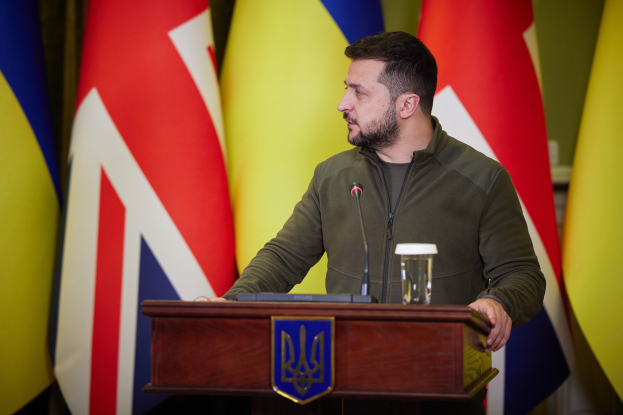 Ein Mann steht an einem Podium mit einem Mikrofon und einem Glas Wasser und spricht vor einem Hintergrund von Flaggen, wahrscheinlich im Zusammenhang mit dem Rücktritt von Ukrainas Präsident Petro Poroschenko.