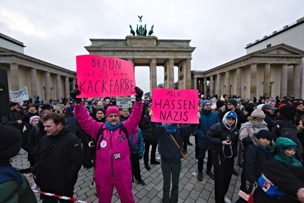 Gruppe von Menschen protestiert vor dem Reichstagsgebäude in Berlin, hält Schilder gegen die Anti-Nazis-Bewegung der deutschen Regierung, mit Gebäuden und Statuen im Hintergrund unter einem klaren blauen Himmel.