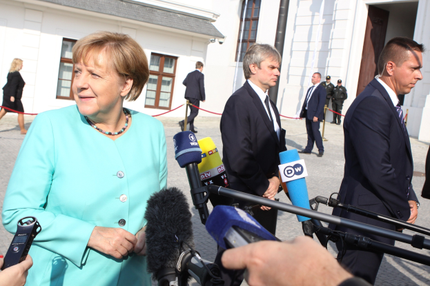 Bundeskanzlerin Angela Merkel spricht vor der Kanzleramt in Berlin mit Reportern umgeben von Menschen mit Mikrofonen im Hintergrund.