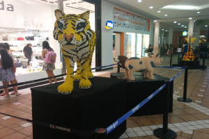 Statuen von Tieren auf schwarzen Kisten umgeben von Pfählen mit Gummigürteln, mit Geschäften, die Taschen, Schuhe und andere Gegenstände ausstellen, und Menschen, die herumlaufen.