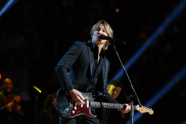 Keith Urban performing on stage at the Joint at Hard Rock Hotel & Casino in Las Vegas, playing guitar with a microphone and band members in the background under dim lighting.