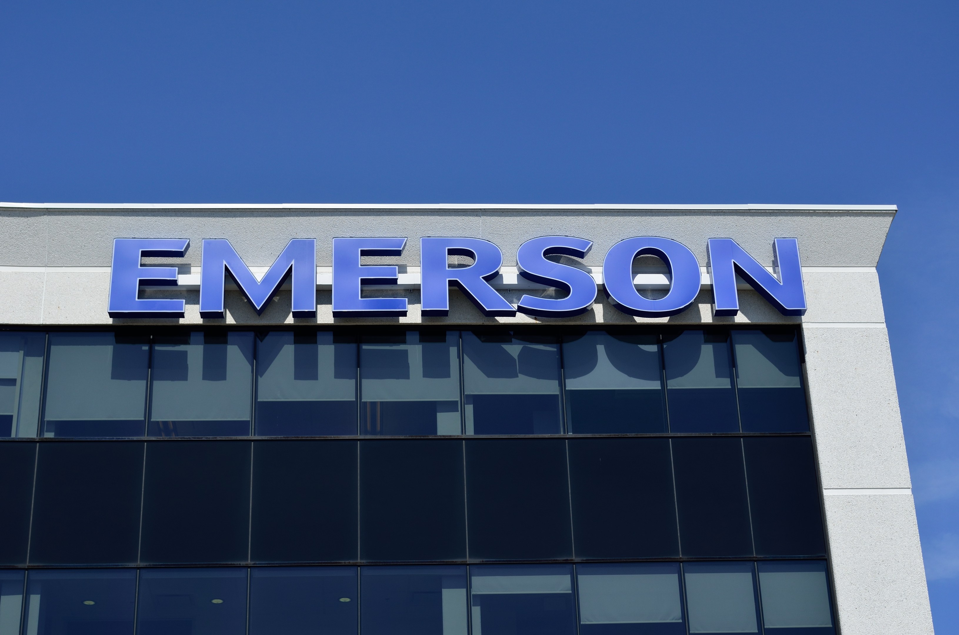 Emerson logo on a building exterior with text stating "Emerson to invest $1.5 billion in the US" against a clear blue sky.