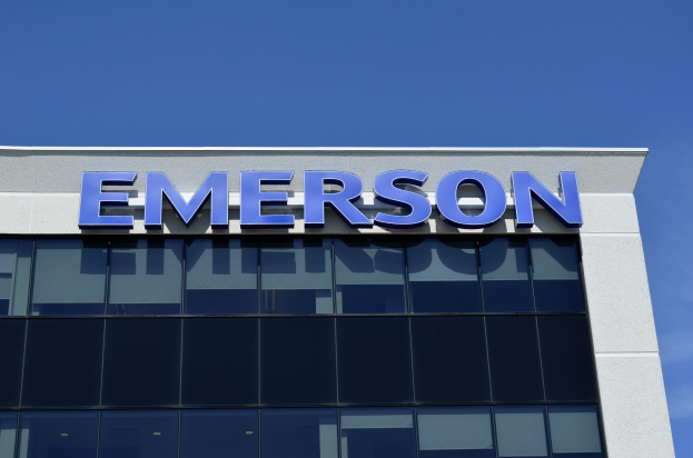 Emerson logo on a building exterior with text stating "Emerson to invest $1.5 billion in the US" against a clear blue sky.
