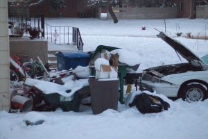 Eine Au√üenszene mit M√ľll in der Mitte, einem Auto auf der rechten Seite, Treppen auf der linken Seite, B√§umen oben und Eis am Boden.