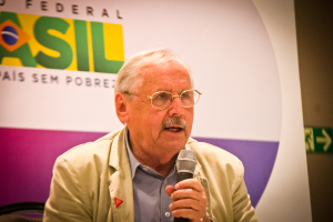 Eine Person, die in ein Mikrofon spricht und von einem Banner mit der Aufschrift 'Bundes' hinter ihr umgeben ist.