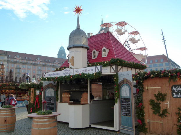 Ein kleines Gebäude mit einem roten Dach und einem Riesenrad davor, umgeben von Menschen und Festschmuck bei einem Oktoberfest-Event in München, Deutschland.