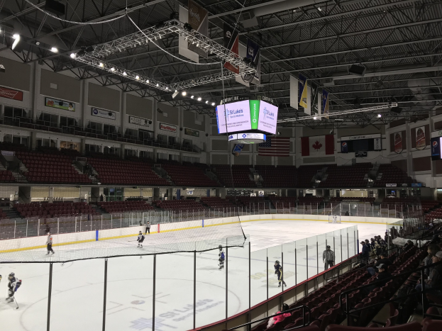 Hockey-Spiel in einer großen Arena mit einem zentralen Netz, Zuschauern auf beiden Seiten, Deckenleuchten und Trägern sowie Wandbannern, die als St. Louis Blues Arena gekennzeichnet sind.