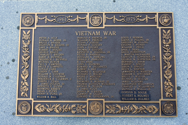Plaque on the side of a building reading "Vietnam War" in bold black lettering, mounted on a dark material with a decorative border.
