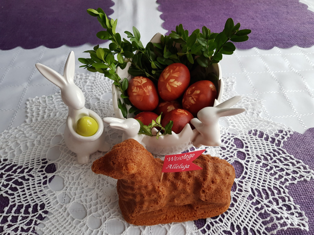 Ein Tisch mit einer Decke darauf h├Ąlt eine Schale mit bunten Ostereiern und Osterhasenfiguren darauf.