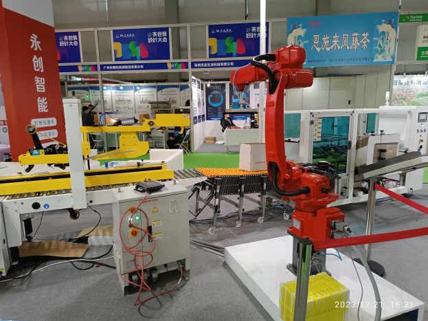 Eine Gruppe von Robotern auf einem Tisch umgeben von Maschinen und Kabeln, mit ein paar Menschen im Hintergrund in einer Fabrikumgebung.