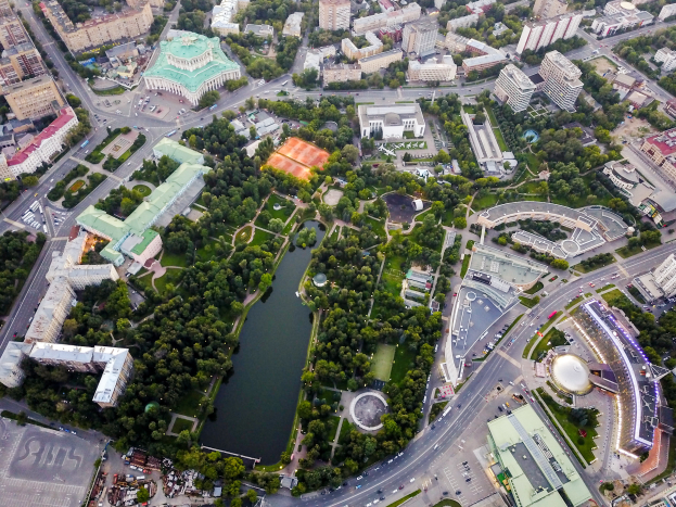 Eine Luftaufnahme einer Stadt mit einem zentralen Park umgeben von Grünflächen, Gebäuden, Straßen, Fahrzeugen und Wasser.