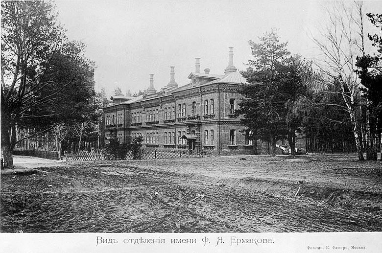 Black and white photo of a large building with windows, a fence, a group of trees, and a cloudy sky, labeled as the Russian Academy of Science and Technology.