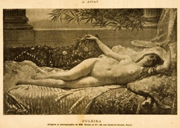 A nude woman reclines on a bed surrounded by pillows and objects, with a tree nearby and text at the bottom.