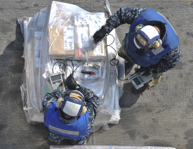 Zwei Männer in blauen Uniformen und Helmen arbeiten an einem großen Drohnenmodell, jeder hält Werkzeuge in den Händen, mit einer Plastikabdeckung auf dem Boden.