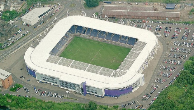 Aerial view of Tottenham Hotspur Football Club's stadium surrounded by city buildings, trees, and roads with vehicles.