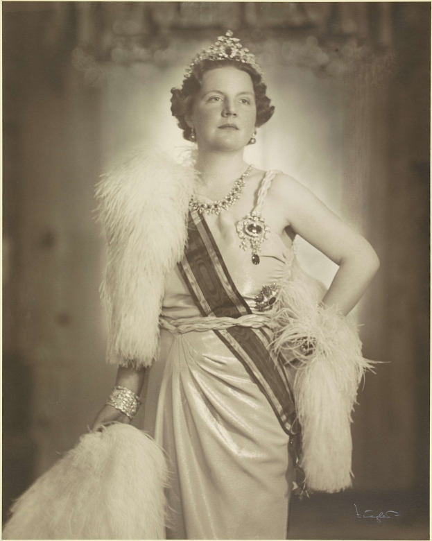 Schwarz-weiß-Foto von Queen Elizabeth II in Kleid und Krone mit unscharfem Hintergrund und Text unten.