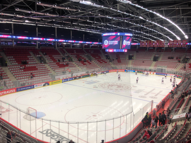Ein Eishockeyspiel in einer großen Arena mit Zuschauern, einem Zaun um die Eisbahn, einem Bildschirm mit der Aufschrift "St. Louis Blues gegen Detroit Red Wings", Metallrahmen und einer Decke mit Deckenleuchten.