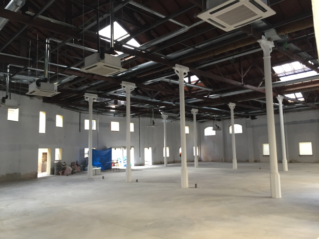 Industrial warehouse space with large windows, pillars, ceiling lights, and air conditioning units, available for rent.