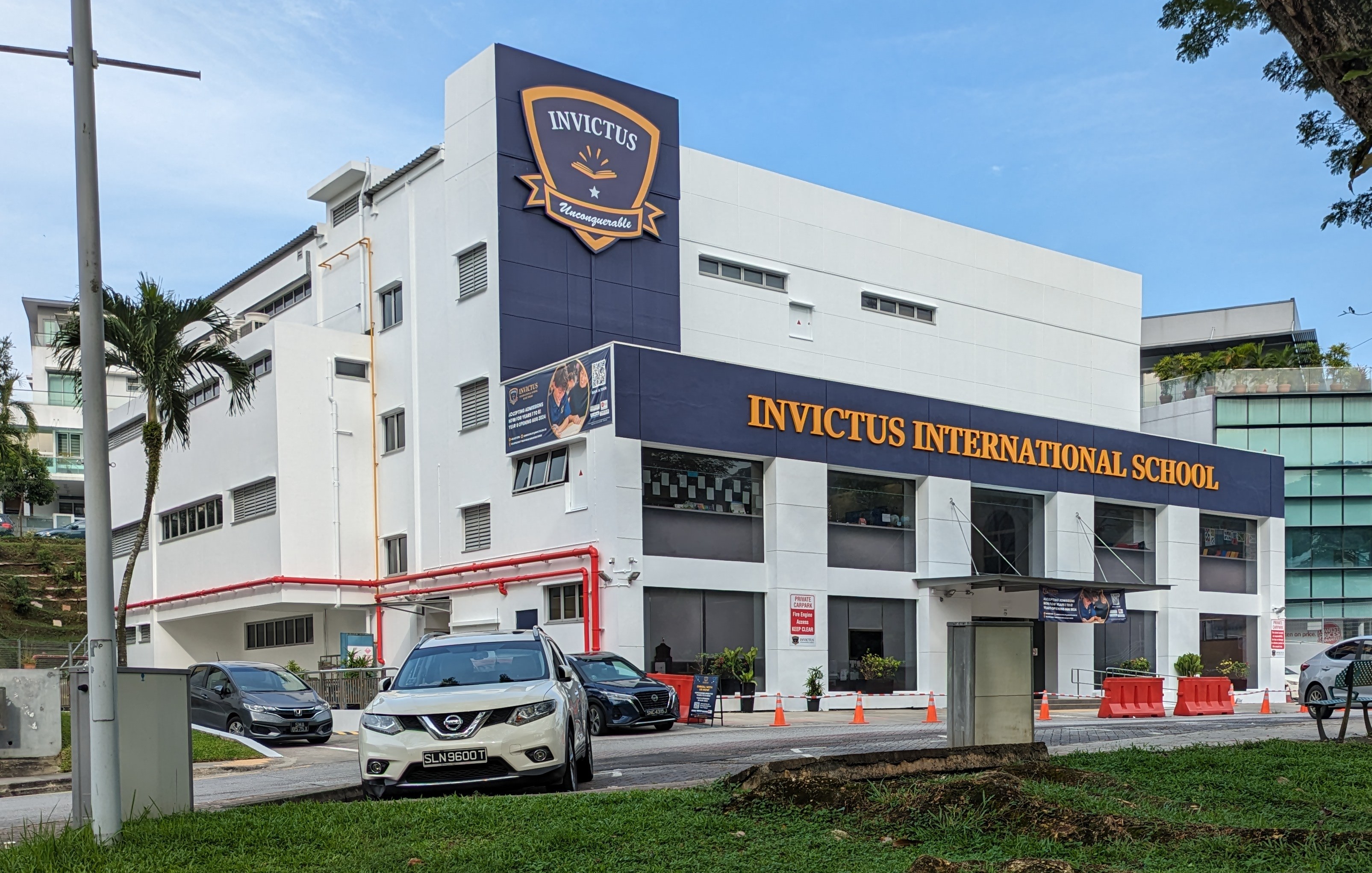 The Invictus International School in Singapore with its buildings, signage, vehicles, road infrastructure, greenery, and sky.