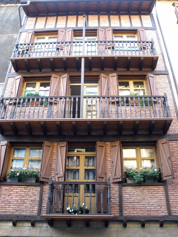 Ein mehrstöckiges Gebäude in Straßburg, Frankreich, mit zahlreichen Fenstern, Balkonen mit Geländern, Türen und Blumentöpfen mit Pflanzen.