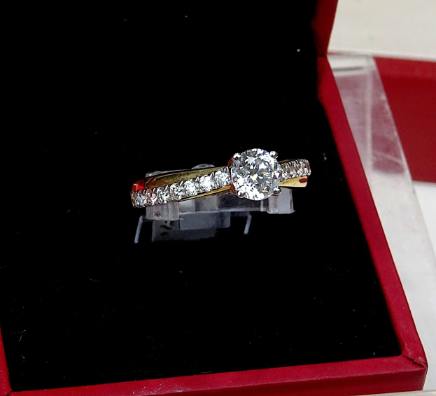 A deep red box containing a diamond engagement ring with a central diamond surrounded by a halo of smaller diamonds, placed on a table.