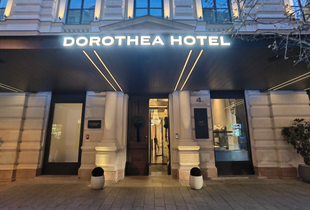 Das Dorothea Hotel in London, England, ein Gebäude mit Glasfenstern und -türen, einem Namen Schild, Topfpflanzen, einem Baum und Deckenleuchten unter einem Dach.