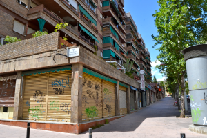 Eine Szene mit Gebäuden, Fenstern, grüner Kleidung, Geschäften, Schildern und umliegenden Bäumen und Pflanzen.