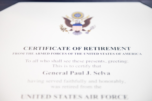 Framed certificate of retirement from the United States Air Force with a blue border, featuring a shield logo with a central star, laurel wreath, and "Retirement" banner in black ink.