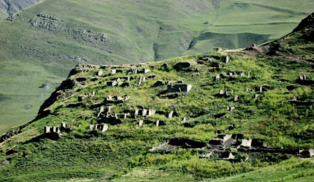 Kleines steinernes Dorf in einem grünen Bergtal mit umgebender Vegetation.