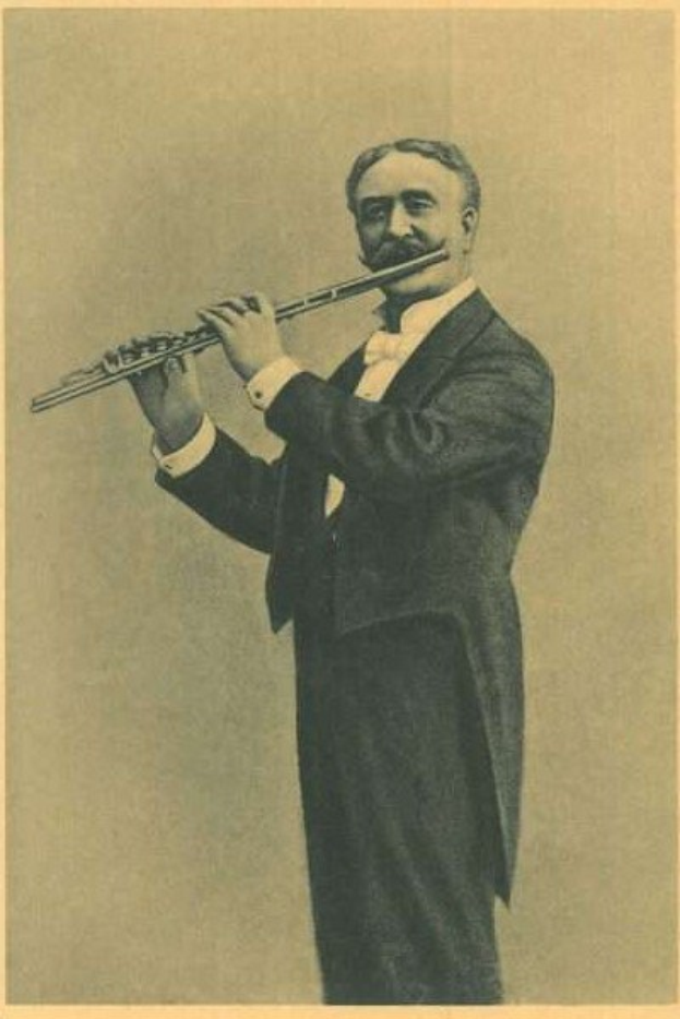 Old black-and-white photograph of a man in a tuxedo playing a flute on stage with eyes closed and serious expression.