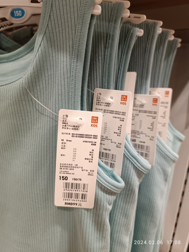 Eine Reihe blauer T-Shirts für Kinder, die an einer Ladengestell hängen, jedes mit einem Preisschild beschriftet "Uniqlo Kids."