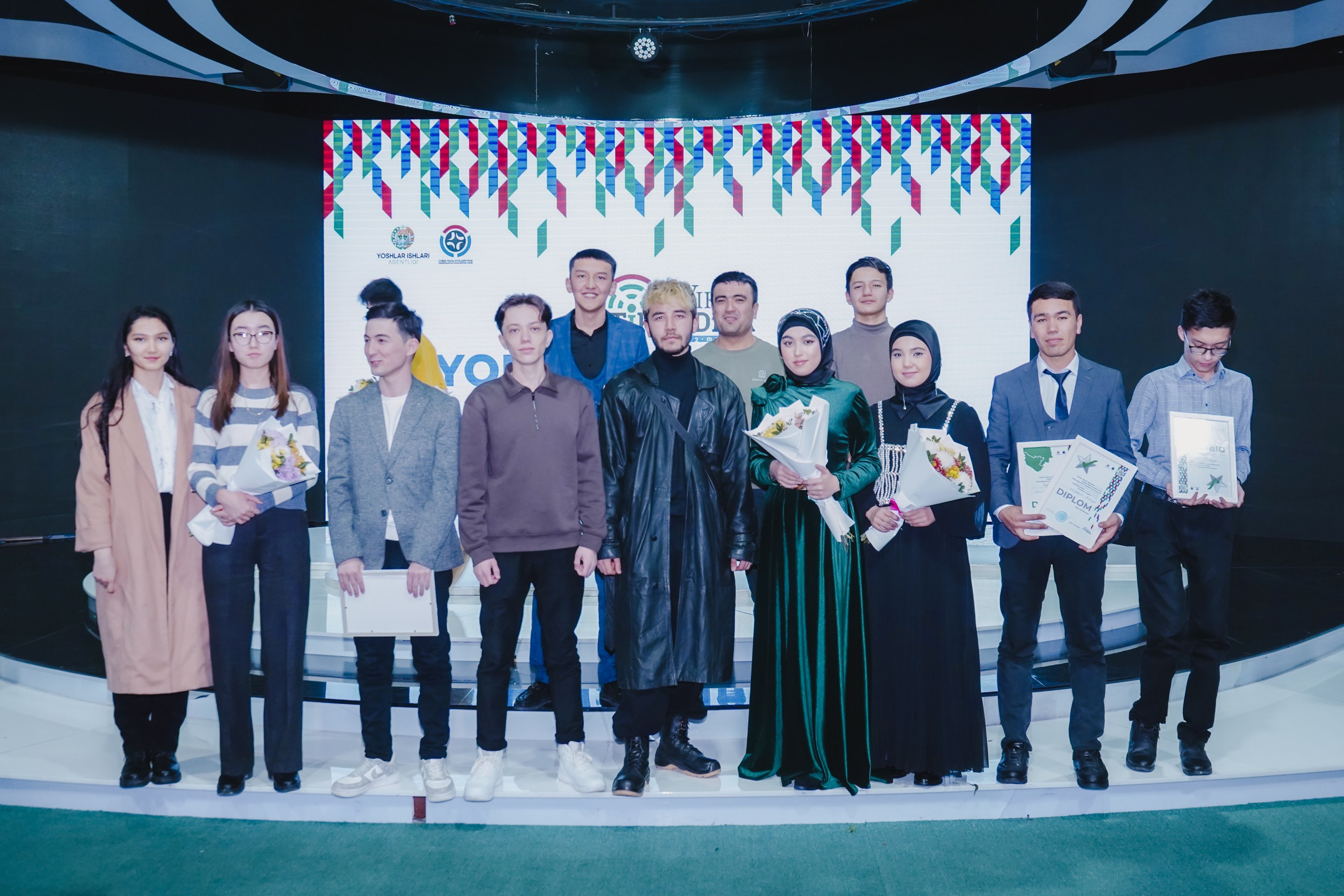 Group of people on a stage holding bouquets and certificates, with a "Youth Solar Awards 2019" banner in the background.