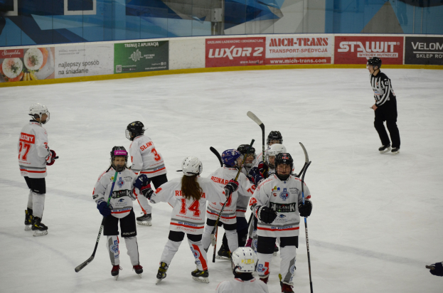 Gruppe junger Menschen, die Eis-Hockey auf einer Indoor-Eisbahn spielen, tragen Helme und halten Hockey-Stöcke, mit einer Person auf der rechten Seite und Texttafeln im Hintergrund.