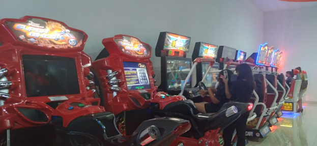 Menschen, die in Stühlen sitzen und Videospiele mit Konsolen vor sich in einem Raum mit einer Wand und einem Boden spielen.