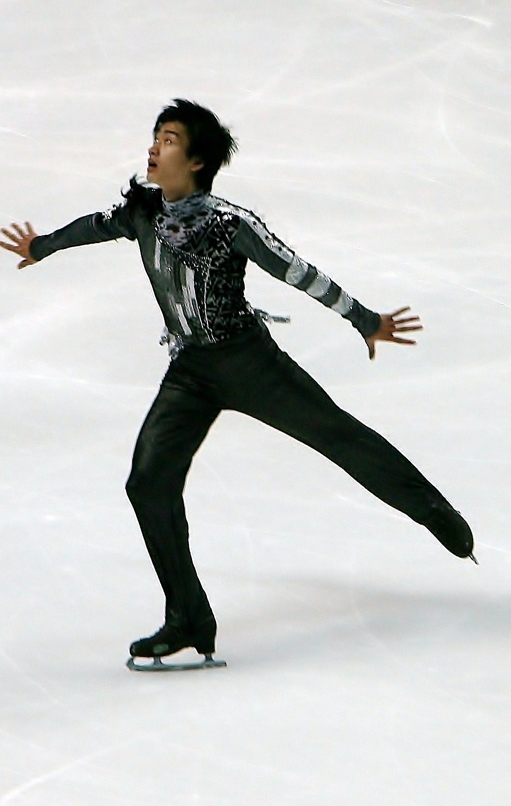 Mann in schwarzer Eiskunstlaufbekleidung gleitet über eine Eisfläche und führt eine Choreographie aus.