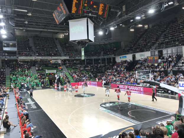 Basketballspiel in einer großen Arena mit Zuschauern, mit einem Spiel zwischen Asvel und Galatasaray, wie auf den Courtside-Boards zu sehen.
