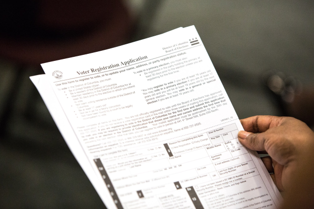 A person holding a voter registration form with blurred background.