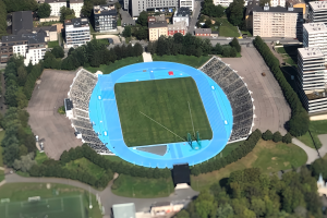 Aerial view of the Olympic Stadium in Munich, Germany, surrounded by city infrastructure including buildings, trees, roads, vehicles, and grass.