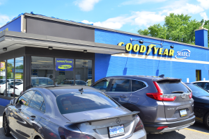 Ein Goodyear Select Autohaus mit mehreren geparkten Autos, das ein Gebäude mit Text und einen Hintergrund aus Bäumen und einem wolkenverhangenen Himmel zeigt.