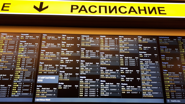 Ein Abflugtafel am Airport mit einem gelben Schild darüber, das Text und Zahlen zu Abflug- und Ankunftszeiten anzeigt.