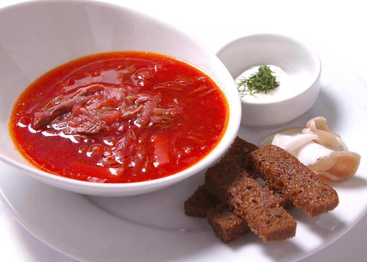 Weißer Teller mit einer Schüssel dicker roter Gazpacho-Suppe, leicht getoastetes Brot und Petersiliengarnitur.