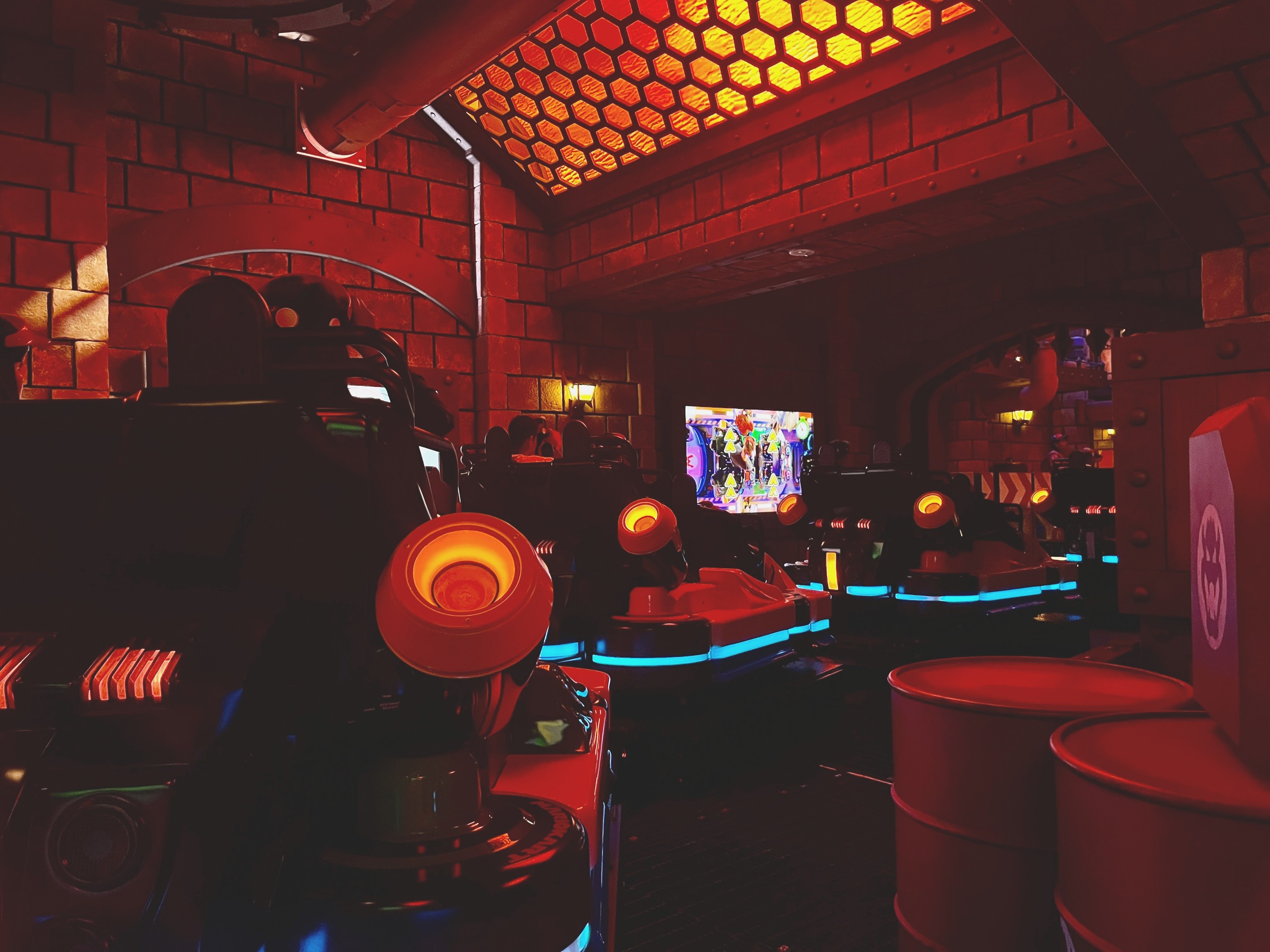 Ein hell erleuchteter Arcade-Raum voller verschiedener Videospielautomaten, ein großer Bildschirm und Deckenleuchten, die eine lebendige Atmosphäre schaffen.