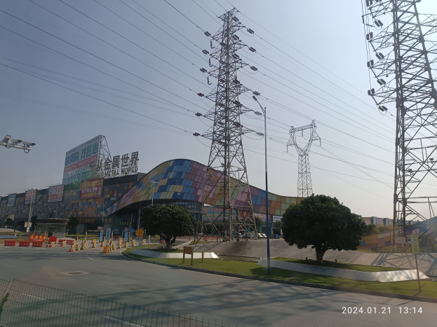 Ein großes Gebäude mit zahlreichen Stromleitungen davor, umgeben von Bäumen, Gras, einer Straße, einem Zaun, Verkehrskegeln und Laternen, mit einem Wasserzeichen unten, wahrscheinlich Teil der Shenzhen Electric Co., Ltd.