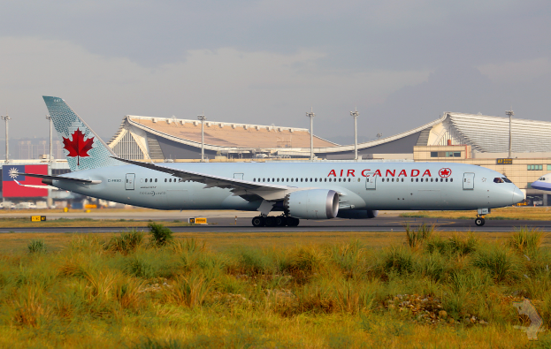 Ein Air Canada Airbus A330-300 auf der Rollbahn des Toronto Pearson International Airport, umgeben von Gras und Pflanzen, mit Gebäuden, Polen und einem klaren blauen Himmel im Hintergrund.