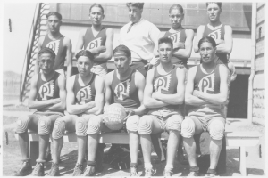 Ein Schwarz-Weiß-Foto einer Basketballmannschaft auf der Bank sitzend, mit einem Mann in der Mitte, der einen Ball hält, und Text unten auf dem Bild.